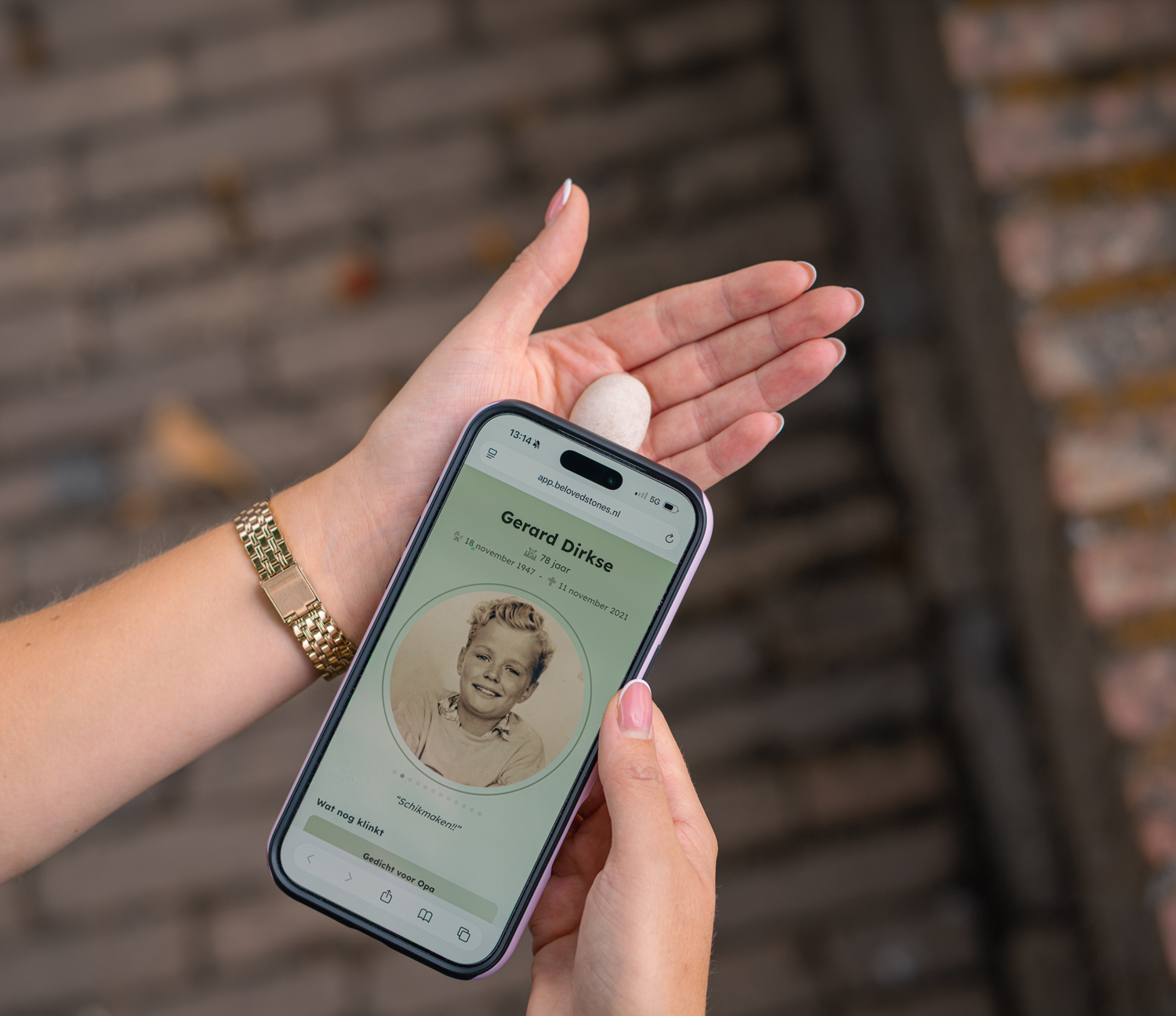 Hand met een steentje tegen een telefoon waarop een herdenkpagina openstaat